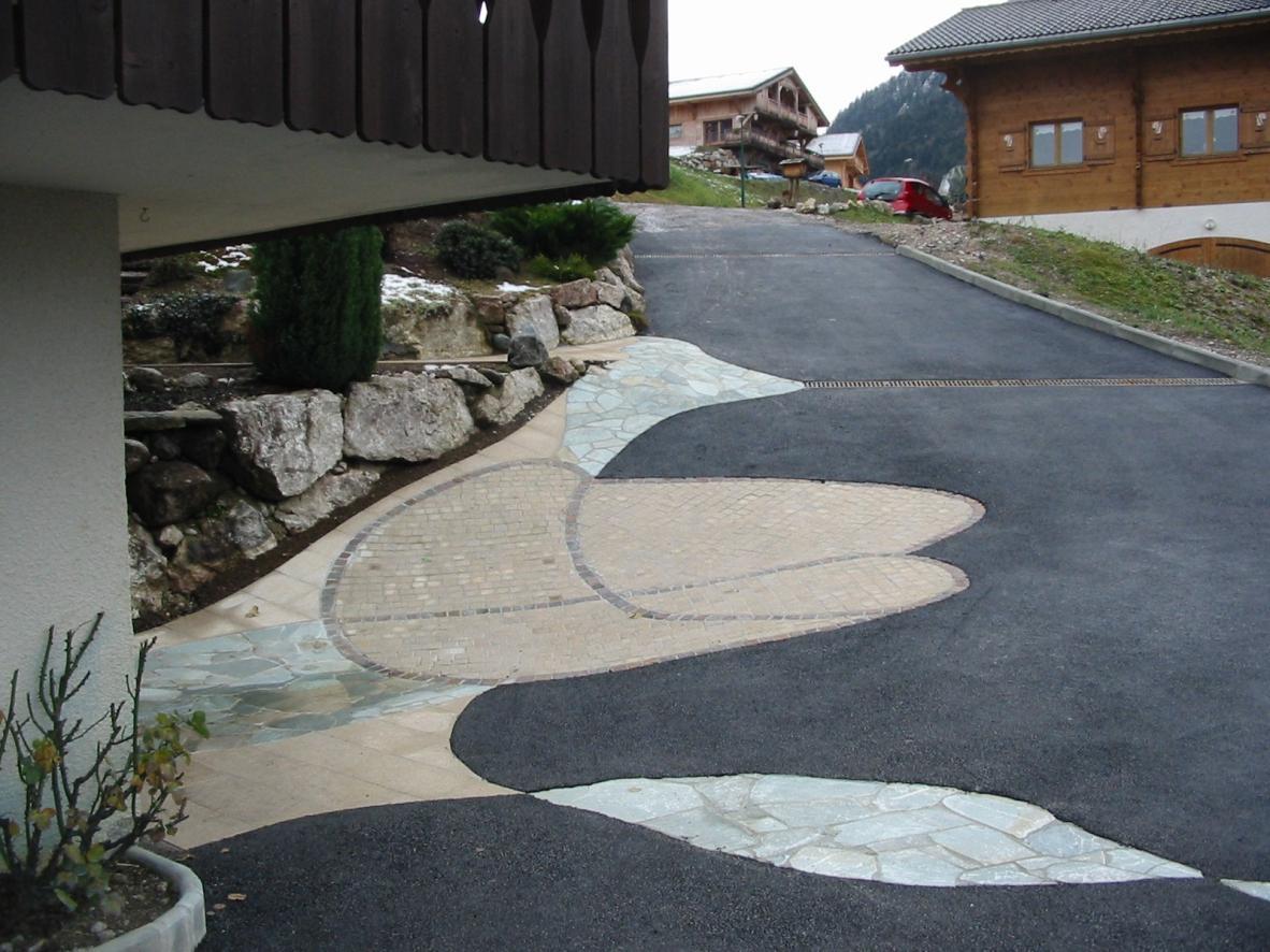 Grand motif en pierre naturelle, pavés et dalles, devant l'accès du garage d'une maison, et enrobé noir tout autour. Réalisation de cette cour à La Vernaz près de Thonon Grand motif en pierre naturelle, pavés et dalles, devant l'accès du garage d'une maison, et enrobé noir tout autour. Réalisation de cette cour à La Vernaz près de Thonon