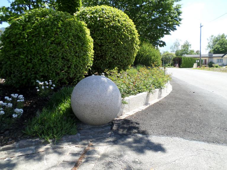 Bordure haute et sphère décorative en pierre pour marquer l'accès.
