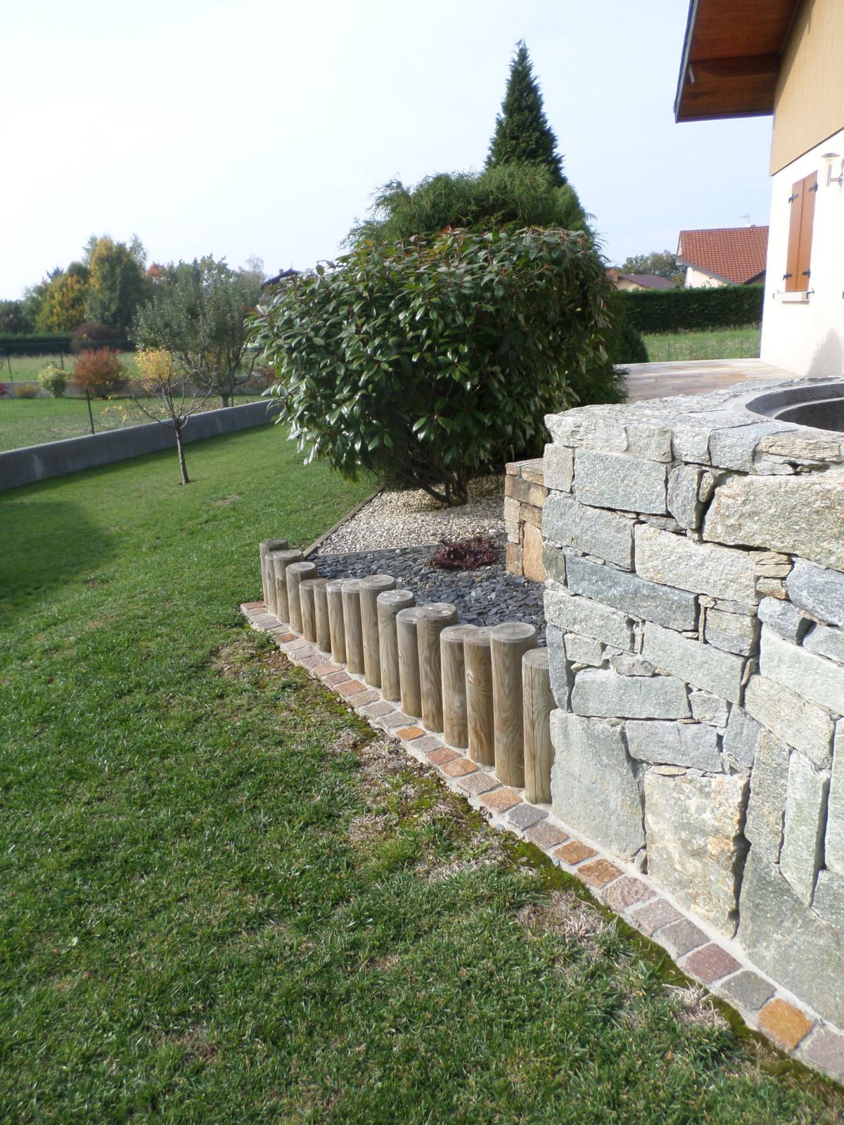 Ajoutée à un ouvrage tel que ce mur en pierre et en bois, la bordure en pavés délimite et facilite l'entretien du jardin. 